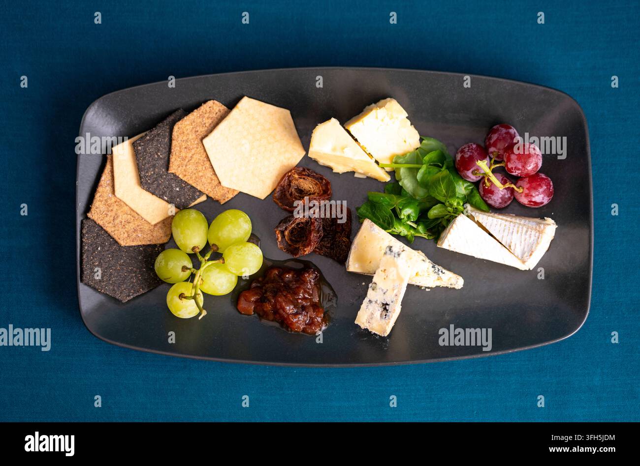 Piatto di formaggi delizioso con uva e cracker assortiti disposti artisticamente Foto Stock
