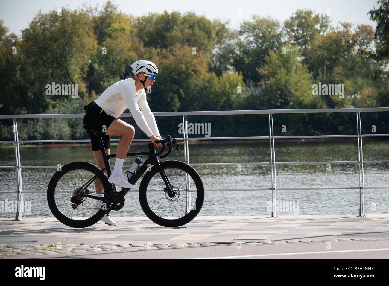 Ciclista su strada maschio in sella a una bicicletta da performance lungo la passeggiata sul lungomare alla luce del giorno, rappresentante l'allenamento di resistenza, la forma fisica e la mobilità attiva. Foto Stock