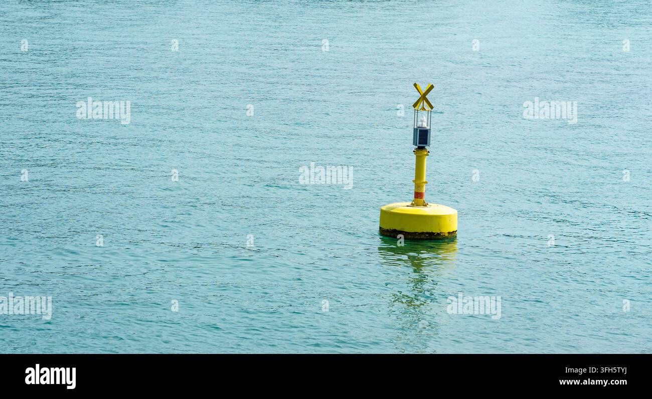 Una boa di navigazione solare gialla galleggia sull'acqua blu con il suo riflesso. Concetto di navigazione, sicurezza, transito, attrezzatura e infrastruttura marina Foto Stock
