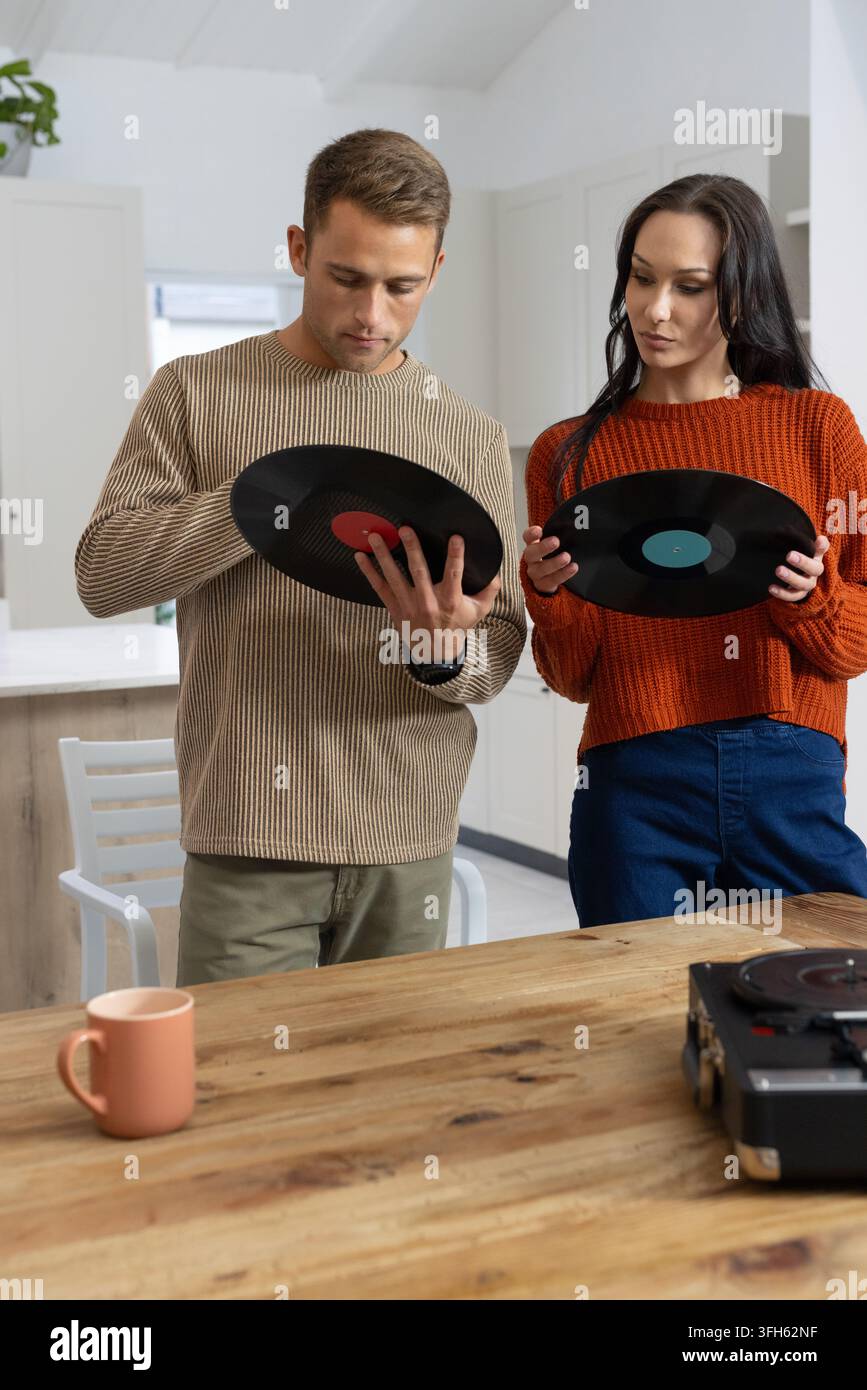 Coppia in maglia che tiene dischi in vinile e controlla le etichette al tavolo della cucina con giradischi Foto Stock