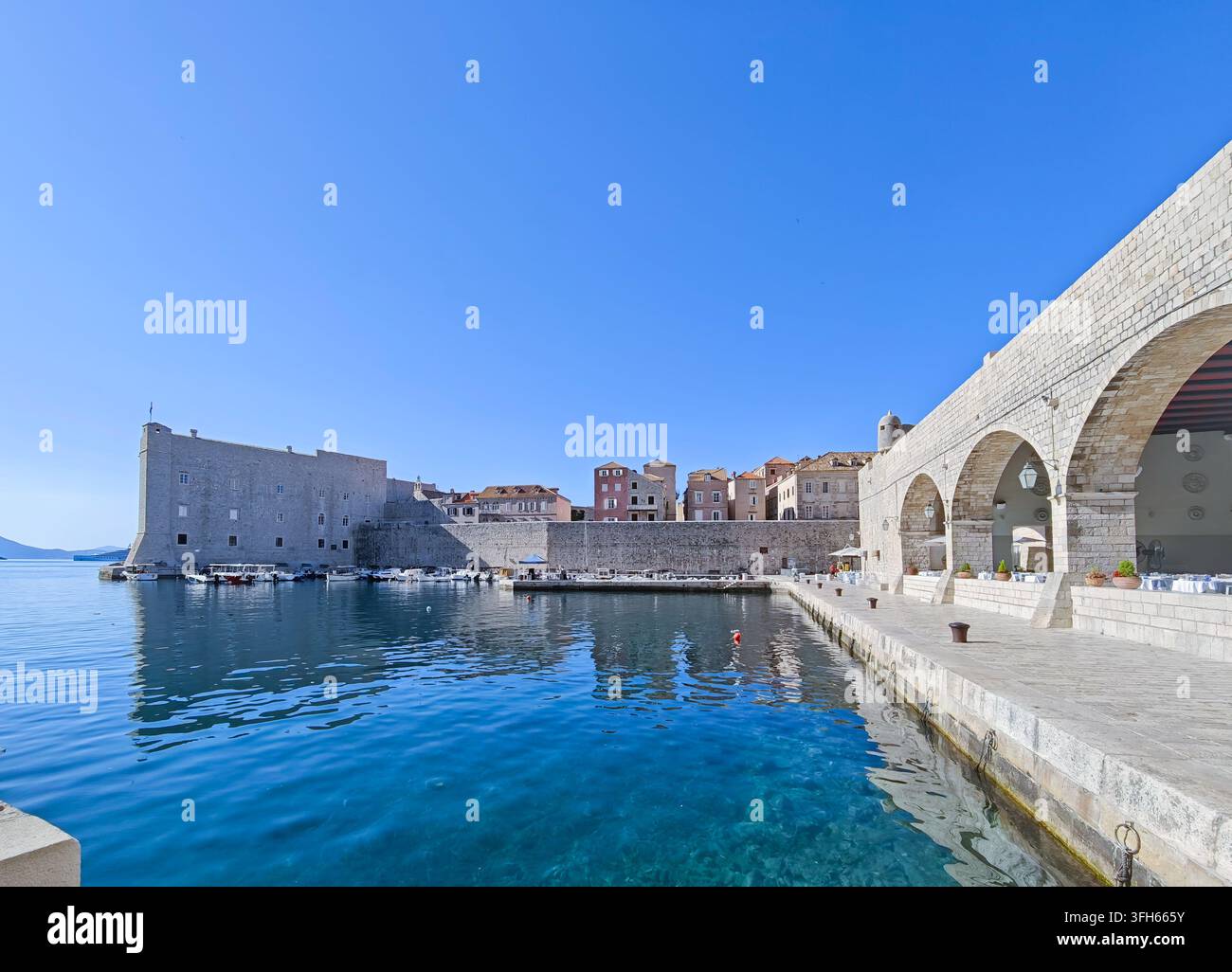 Una tranquilla giornata soleggiata al porto storico di Dubrovnik, che mostra acque blu chiare, antiche fortificazioni in pietra e il fascino costiero. Foto Stock