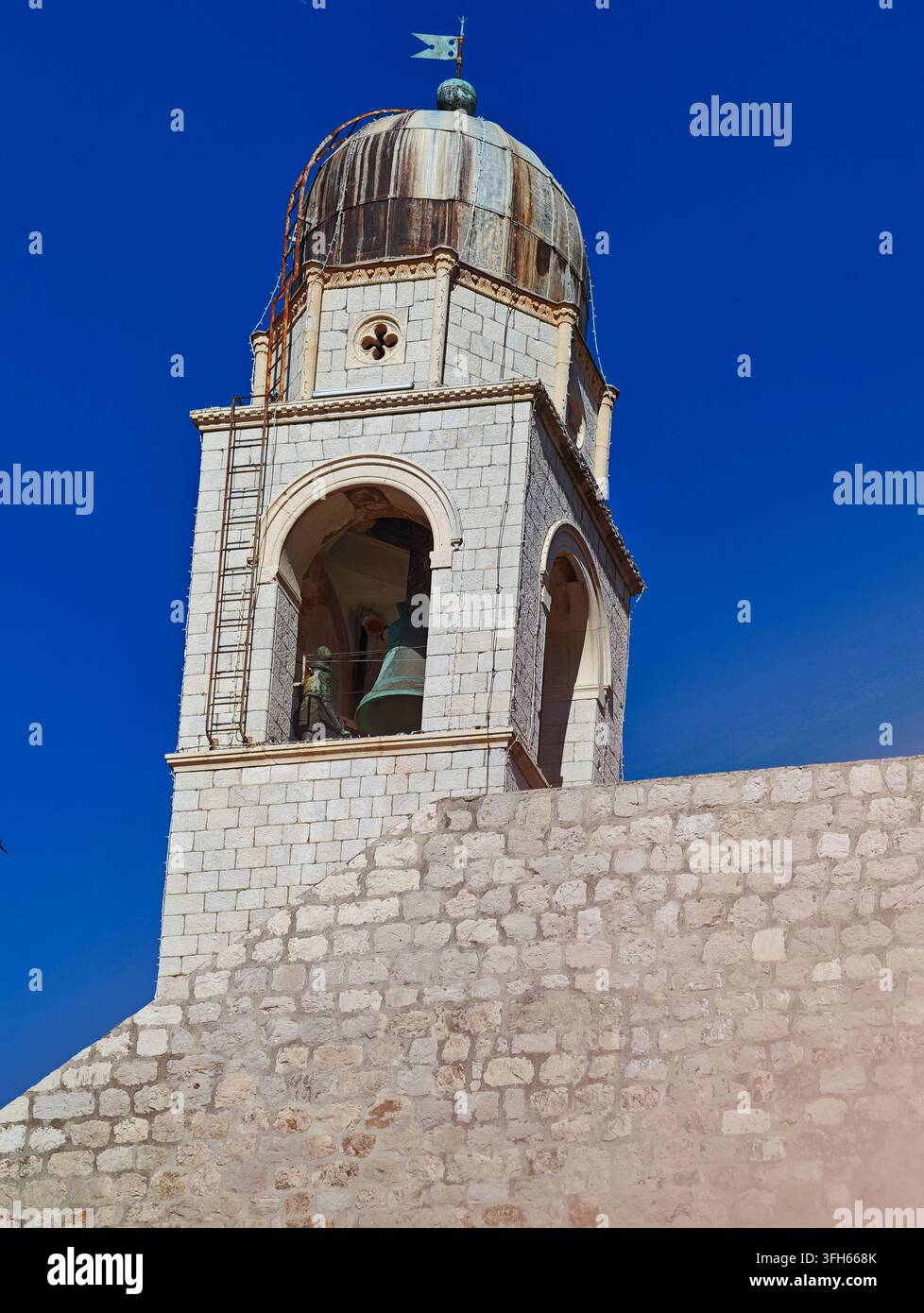 Una vista pittoresca del torre campanaria storica di Dubrovnik con pietra ammuffita, una grande campana in bronzo e cieli azzurri. Foto Stock