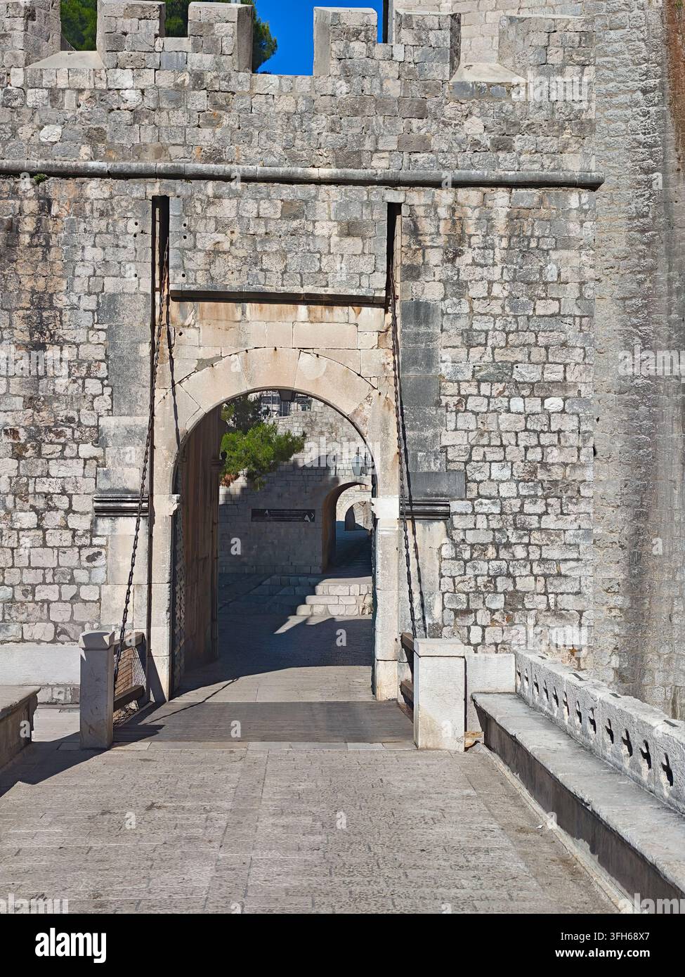 Una giornata soleggiata che mette in risalto le mura di pietra erose, l'ingresso ad arco e le catene del ponte levatoio della storica fortezza della Porta di Ploce. - Immagine stock catturata con smartphone