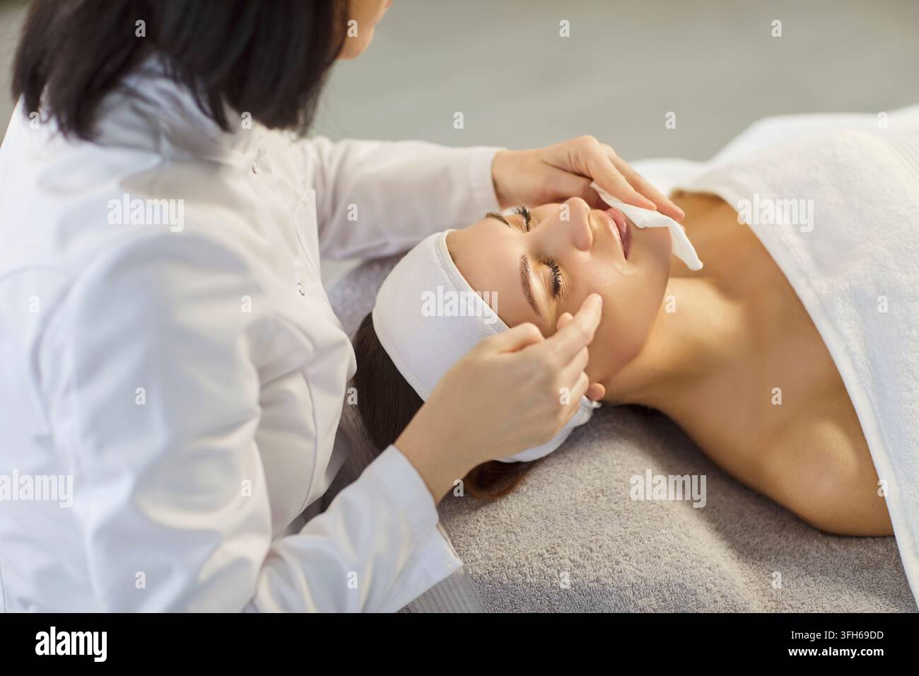 Donna cosmetologa che utilizza salviette umidificate con acqua micellare per preparare il viso dei clienti ai trattamenti di bellezza Foto Stock