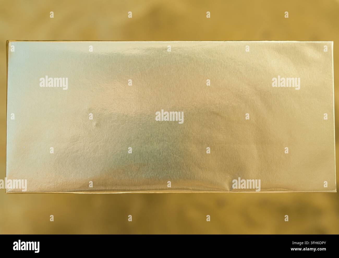 Barretta di cioccolato vuota avvolta in carta stagnola su sfondo dorato, modello di confezione. Vista dall'alto. Minimal. Spazio per il testo. Profondità di campo ridotta. Foto Stock