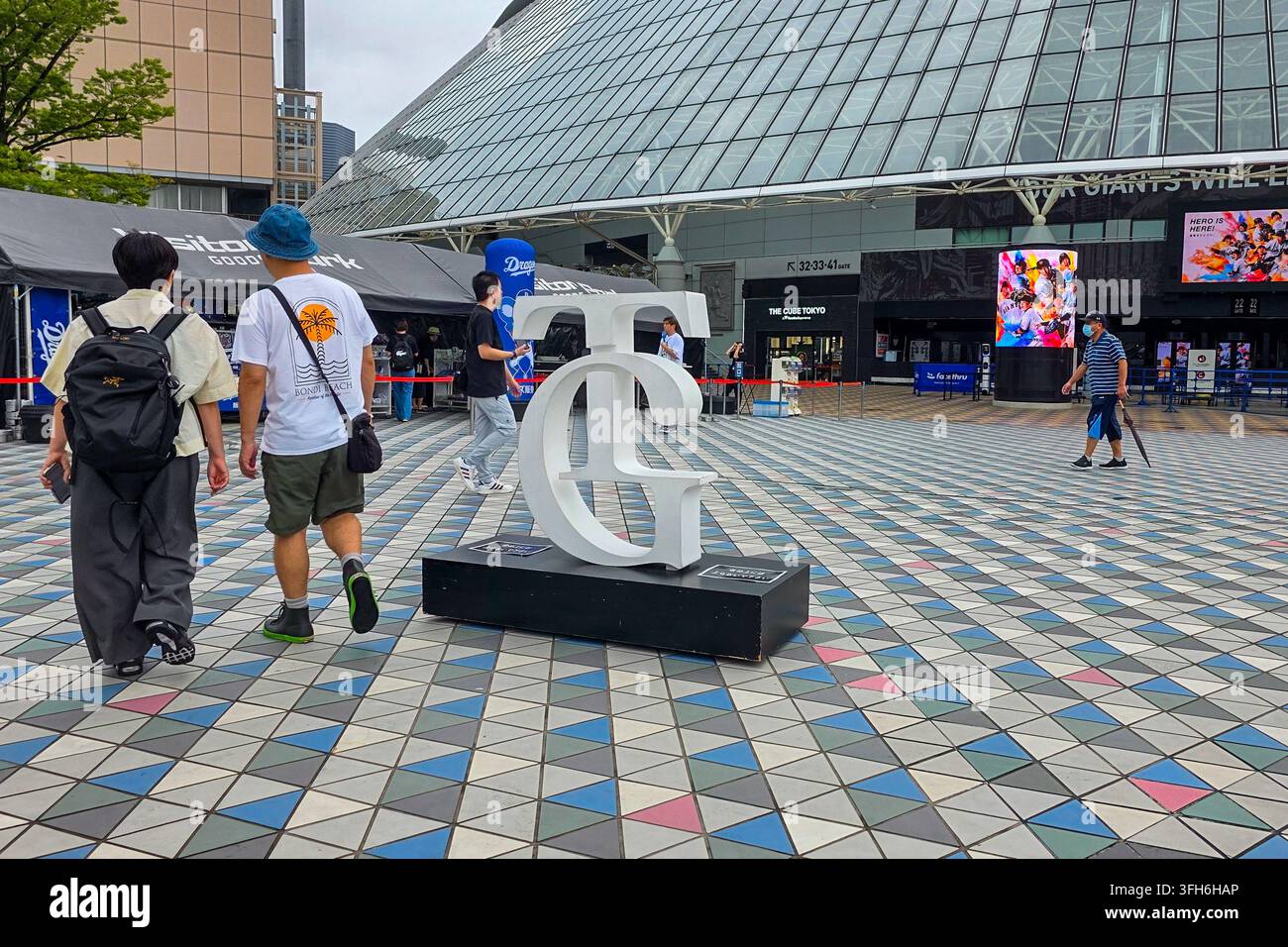 Tokyo, Giappone – 17 luglio 2026: Scultura del logo TG dei Tokyo Giants all'esterno del Tokyo Dome, con visitatori, esposizioni di eventi e strutture dello stadio intorno all'ingresso Foto Stock