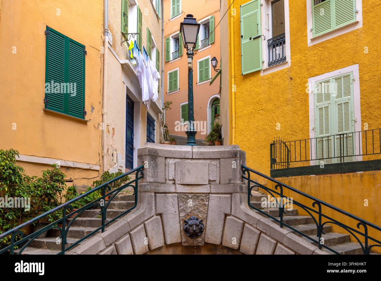 Facciate mediterranee colorate, finestre con persiane chiuse e scale in pietra incorniciano una tranquilla strada del centro storico a Villefranche-sur-Mer sulla costa della Costa Azzurra Foto Stock