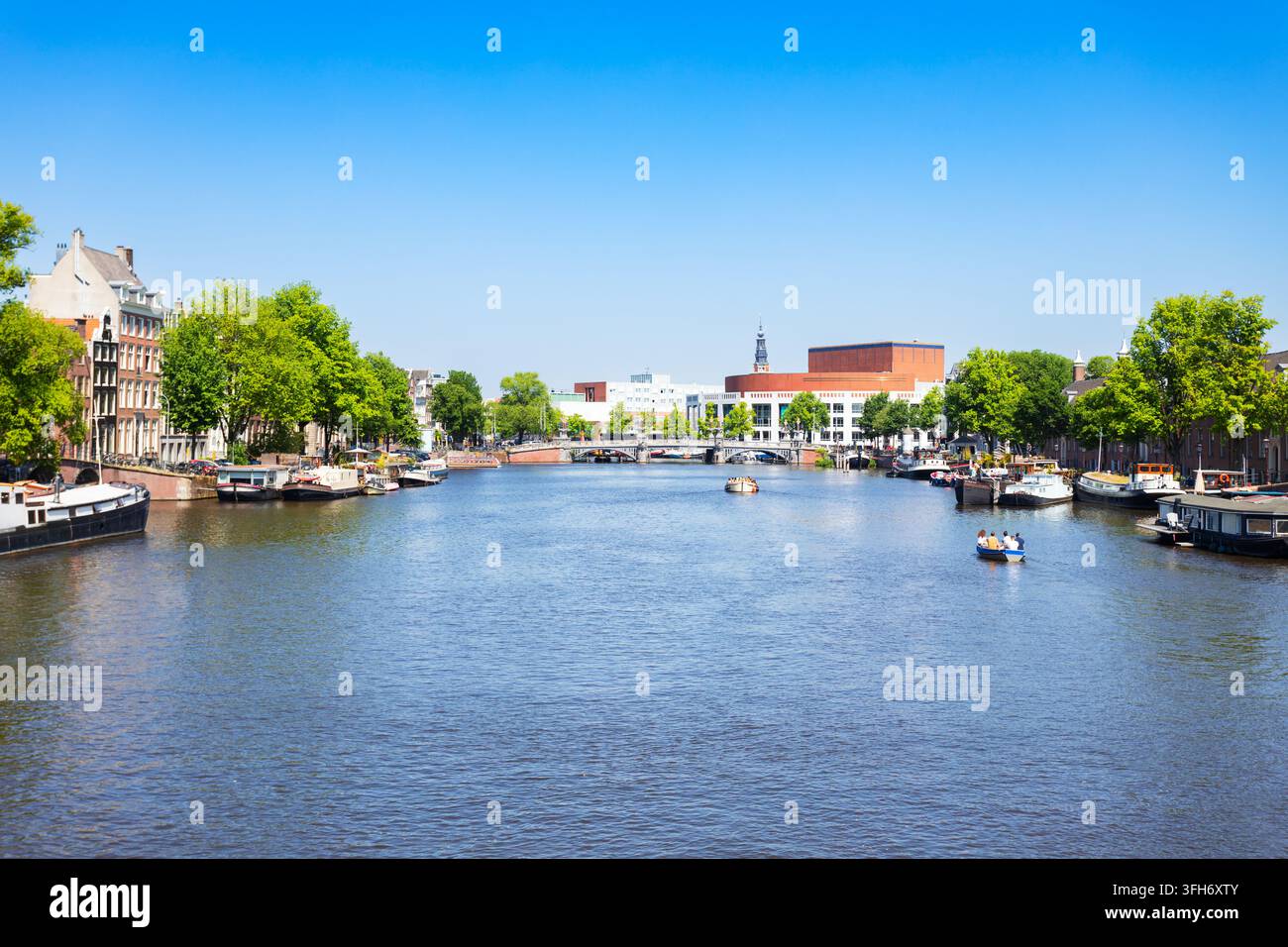 Vista del fiume Amstel con motoscafi e storiche case sui canali di Amsterdam, Paesi Bassi Foto Stock