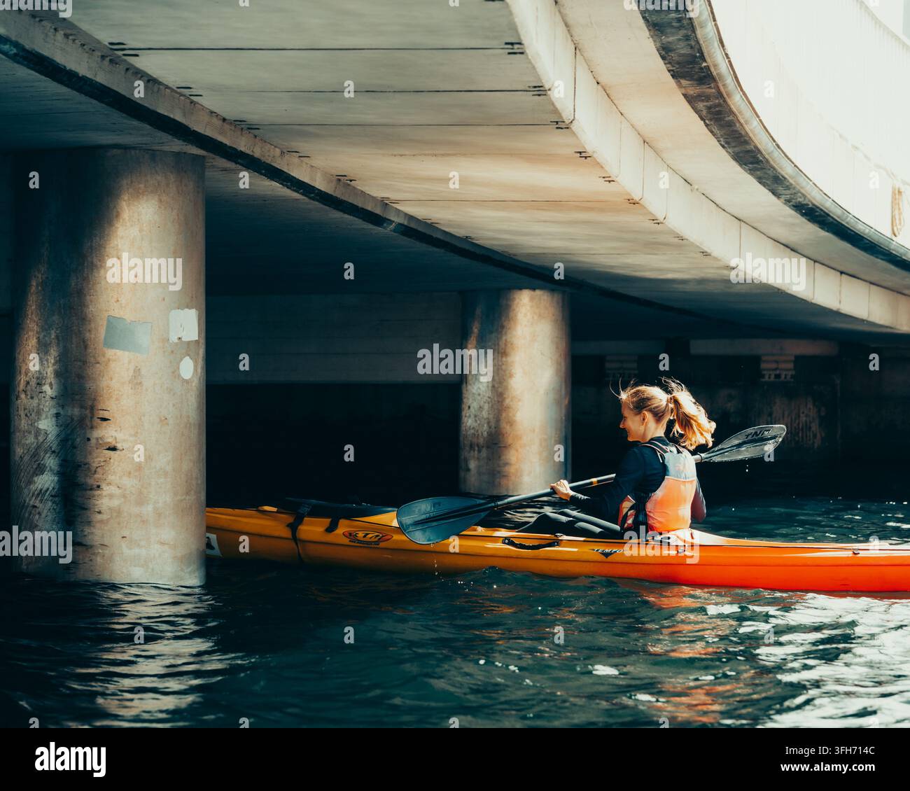 Una donna fa kayak sotto un ponte nel porto di Copenaghen, Danimarca. Foto Stock