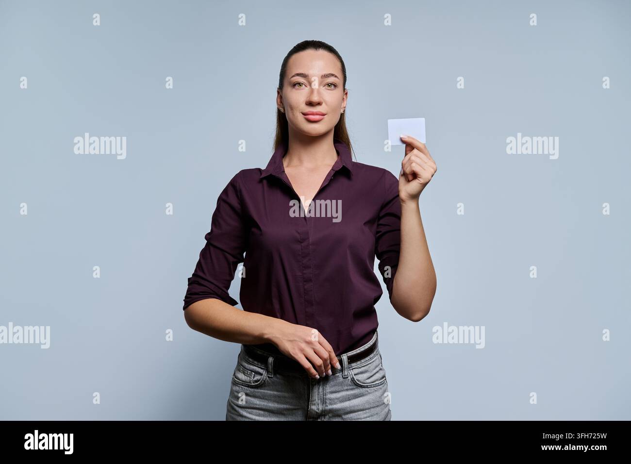 Giovane donna d'affari che tiene una carta di plastica vuota guardando la telecamera su sfondo grigio Foto Stock