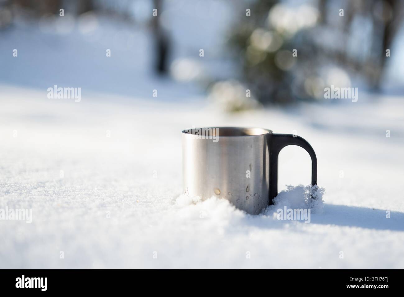 Bicchiere di metallo con bevanda calda in piedi nella neve fresca in una giornata invernale soleggiata. Utile per viaggi invernali, attività ricreative all'aperto, bevande calde e condizioni meteorologiche fredde con Foto Stock