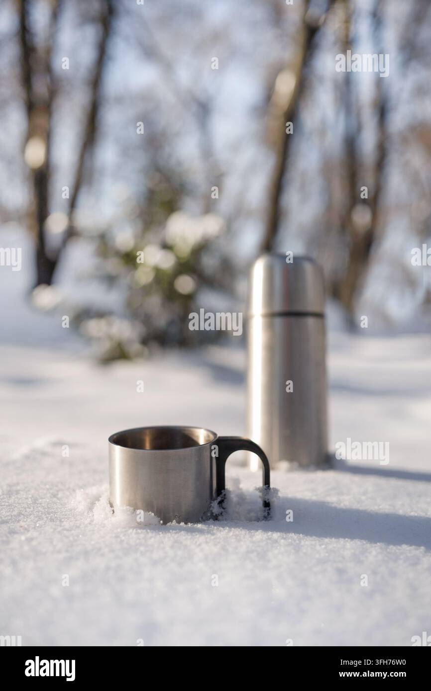 Termos in acciaio inossidabile e tazza in metallo in piedi nella neve profonda all'aperto. Utile per viaggi invernali, bevande calde, escursioni, campeggio e pubblicità in caso di freddo Foto Stock