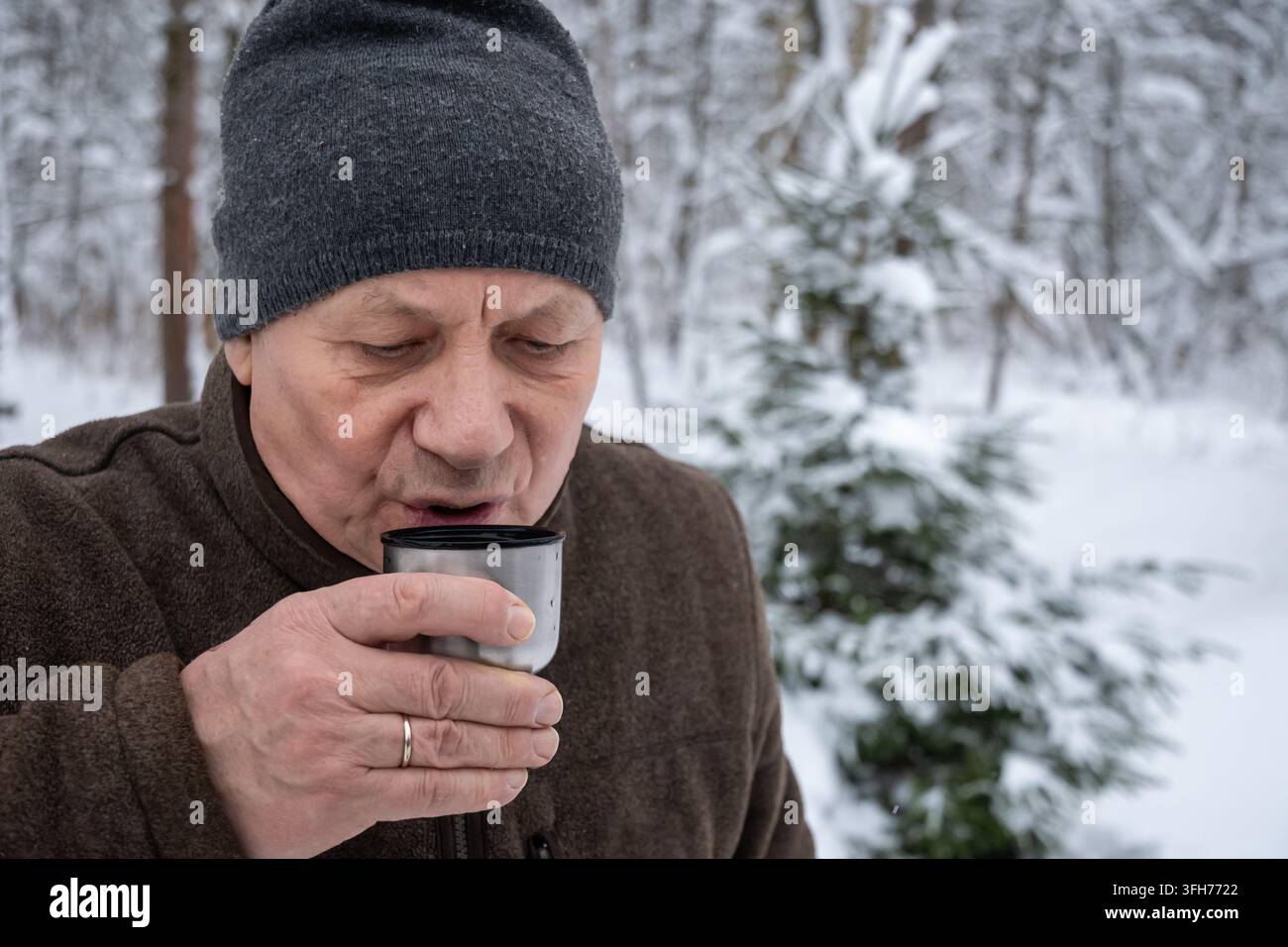 Anziano che si riscalda con una bevanda calda all'aperto in inverno. Utile per concetti di salute in caso di freddo, riscaldamento, invecchiamento attivo e stile di vita invernale. Foto Stock