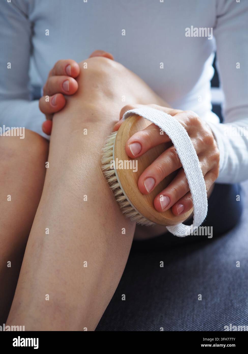 Donna matura si spazza la gamba a secco a casa come parte di una routine di cura personale e benessere Foto Stock