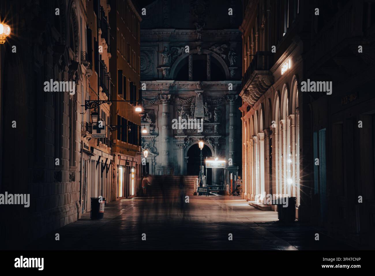 I pedoni passano attraverso una stretta via illuminata vicino alla Piazza San Marco a Venezia, in Italia, di notte. Foto Stock