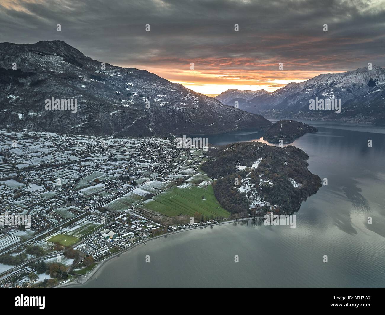 Vista aerea della città di Colico situata sulle rive del Lago di Como con montagne coperte di neve e un cielo al tramonto vibrante a Colico, Lombardia, Italia. Foto Stock