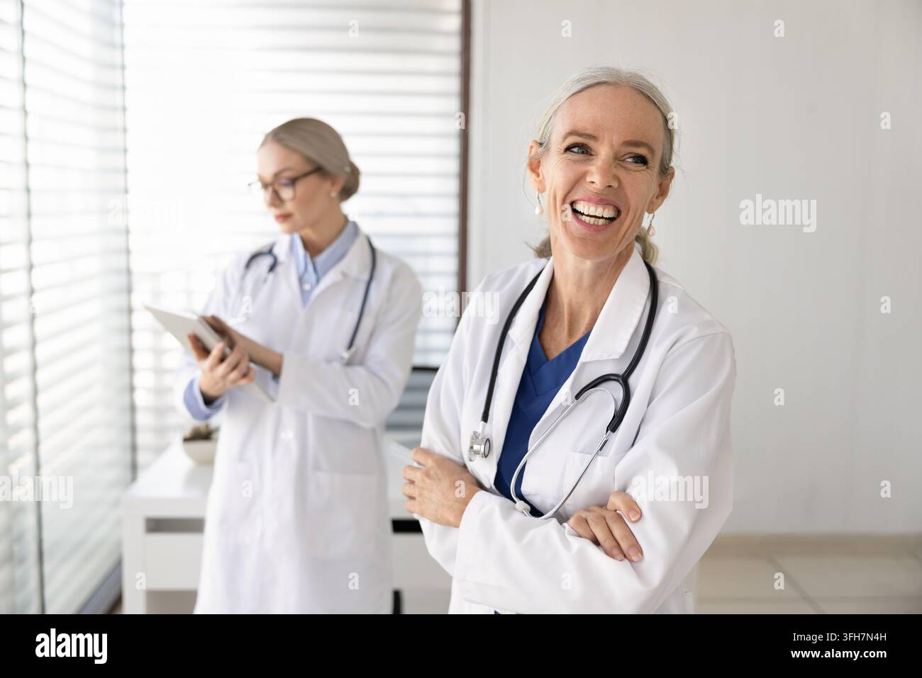 Donna medico di mezza età sicura di sé che ride in piedi nell'ufficio medico della clinica Foto Stock