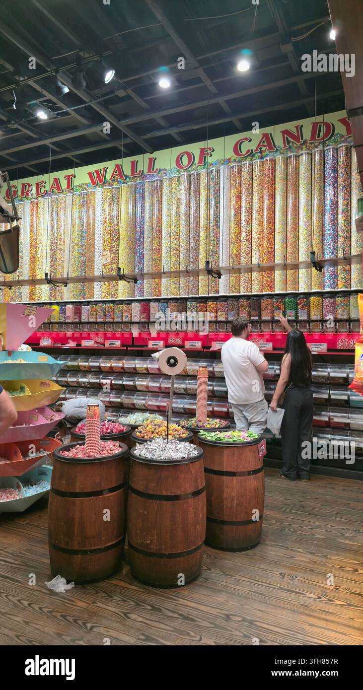 I clienti sfogliano un muro colorato di distributori di caramelle all'interno di una grande negozio di dolciumi - Immagine stock catturata con smartphone