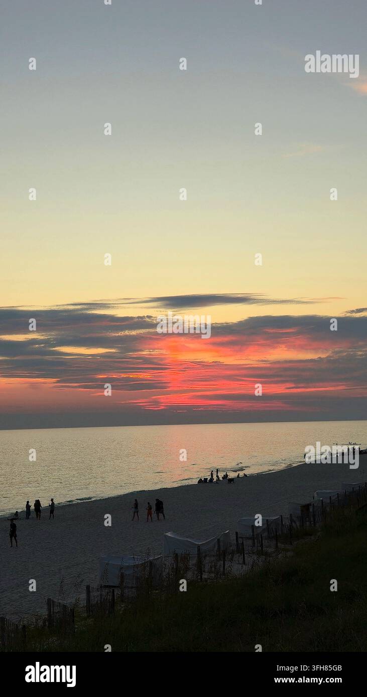 Le persone si godono una spiaggia della Florida al tramonto sotto drammatiche nuvole rosse e arancioni - Immagine stock catturata con smartphone