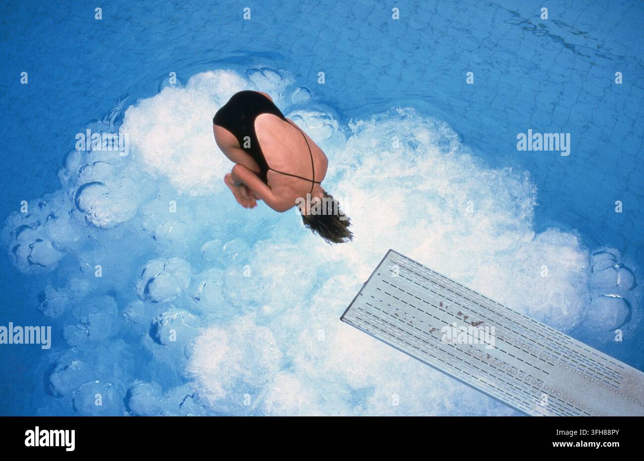 Un'atleta femminile raggomitolata in posizione tuck, che si prepara a distendersi ed eseguire un ingresso pulito in acqua durante una competizione di tuffi. Foto Stock