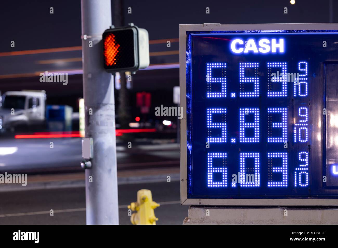 Flusso di traffico serale dietro un tabellone con prezzi alti della benzina. Foto Stock