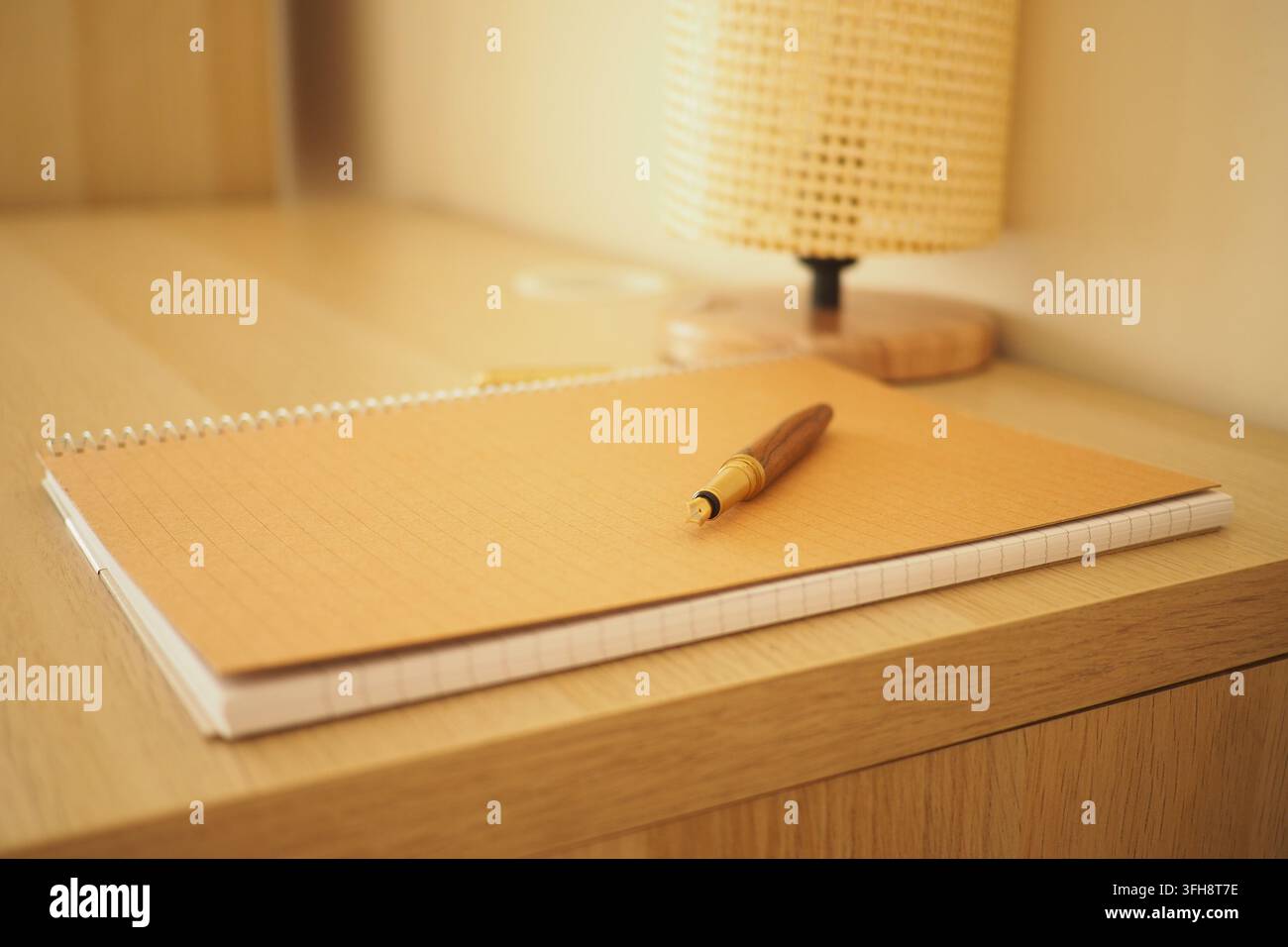 Spazio di lavoro con un quaderno e una penna su una scrivania di legno e una lampada Foto Stock