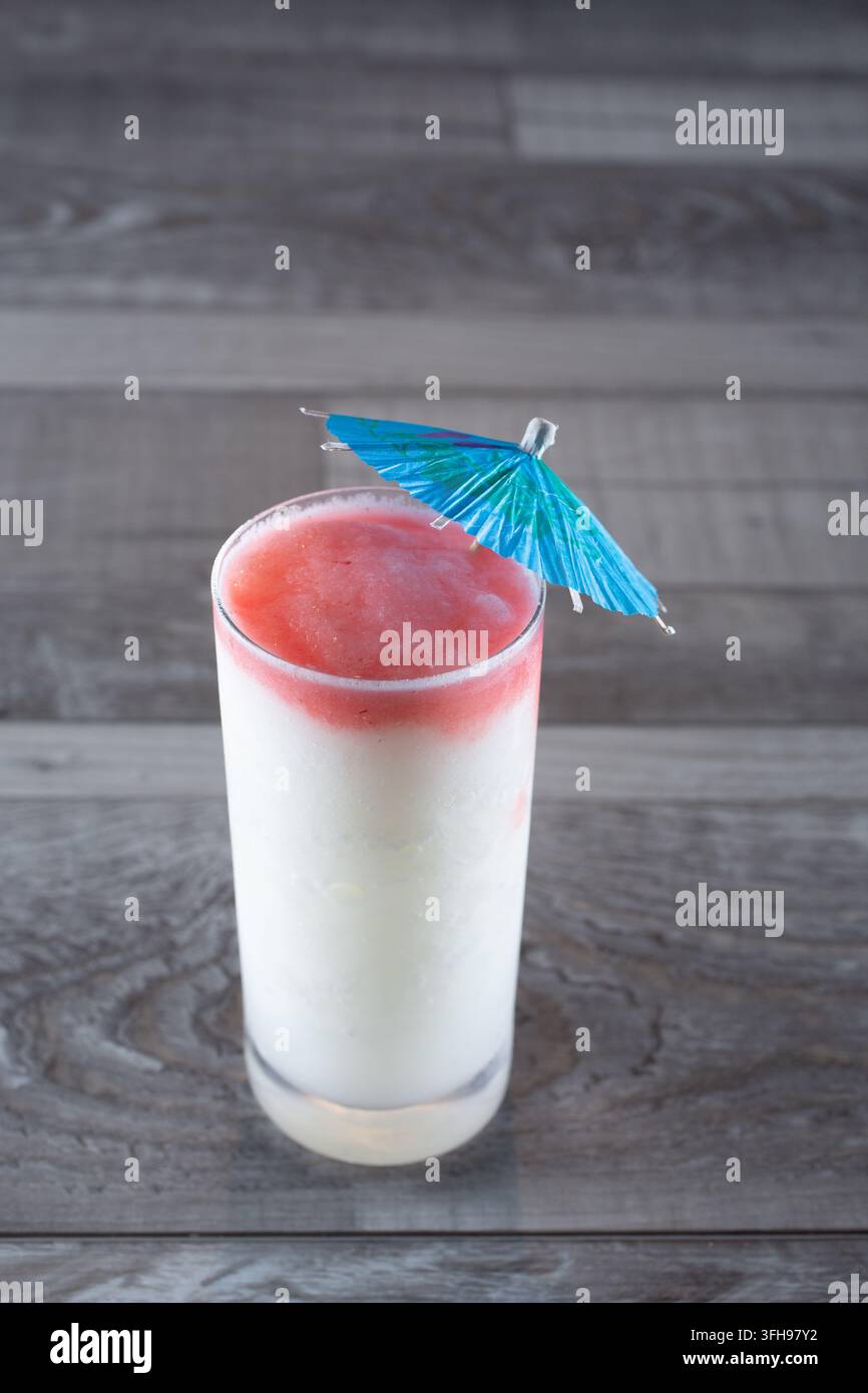 Una vista di una bevanda cocktail ghiacciata bianca, ricoperta da uno strato di sciroppo rosso, guarnita con un ombrellino. Foto Stock