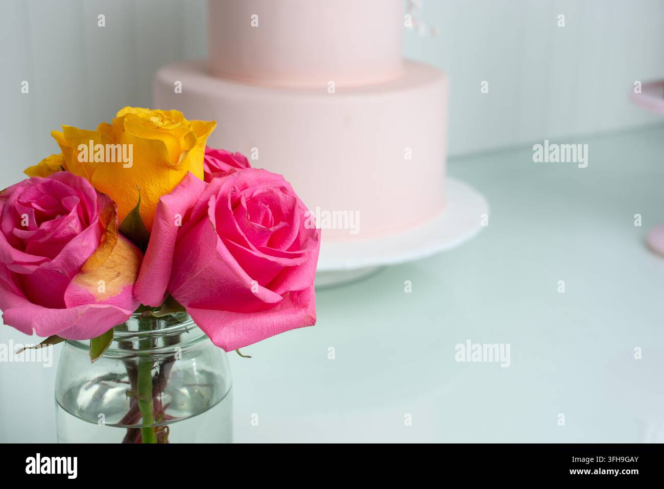 Una vista di rose dai colori brillanti in un vaso, con una torta al fondente rosa sullo sfondo. Foto Stock