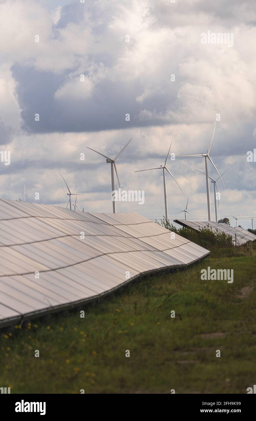 Pannelli solari e turbine eoliche su un sito rurale erboso sotto nuvole imponenti, generazione combinata di energia solare ed eolica. Foto di alta qualità Foto Stock
