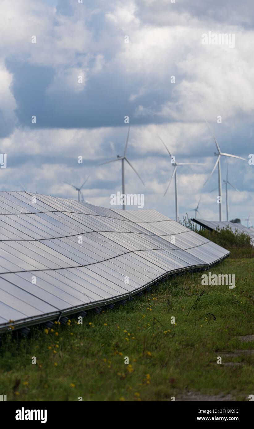 Pannelli solari e turbine eoliche su un sito rurale erboso sotto nuvole imponenti, generazione combinata di energia solare ed eolica. Foto di alta qualità Foto Stock