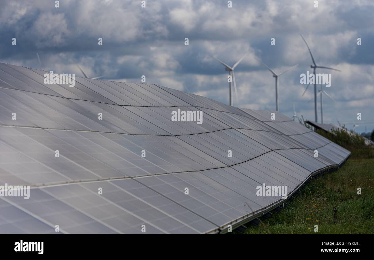 Panelli solari e turbine eoliche che generano energia rinnovabile in un paesaggio rurale sotto nuvole drammatiche. Foto di alta qualità Foto Stock