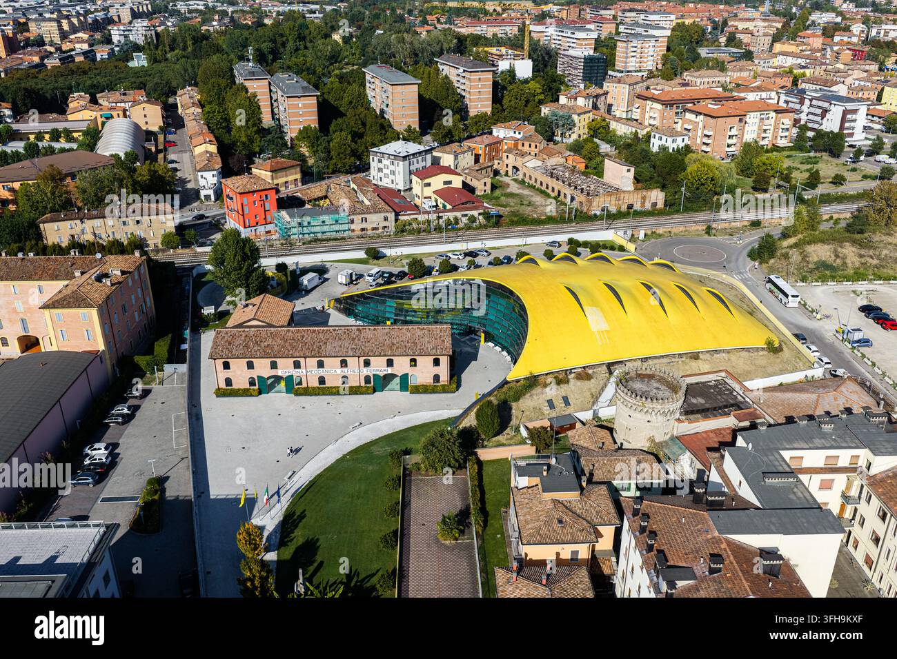 Vista aerea del Museo Enzo Ferrari con il suo tetto giallo distintivo e la facciata moderna in vetro adiacente a un edificio storico in mattoni a Modena, Emilia Foto Stock