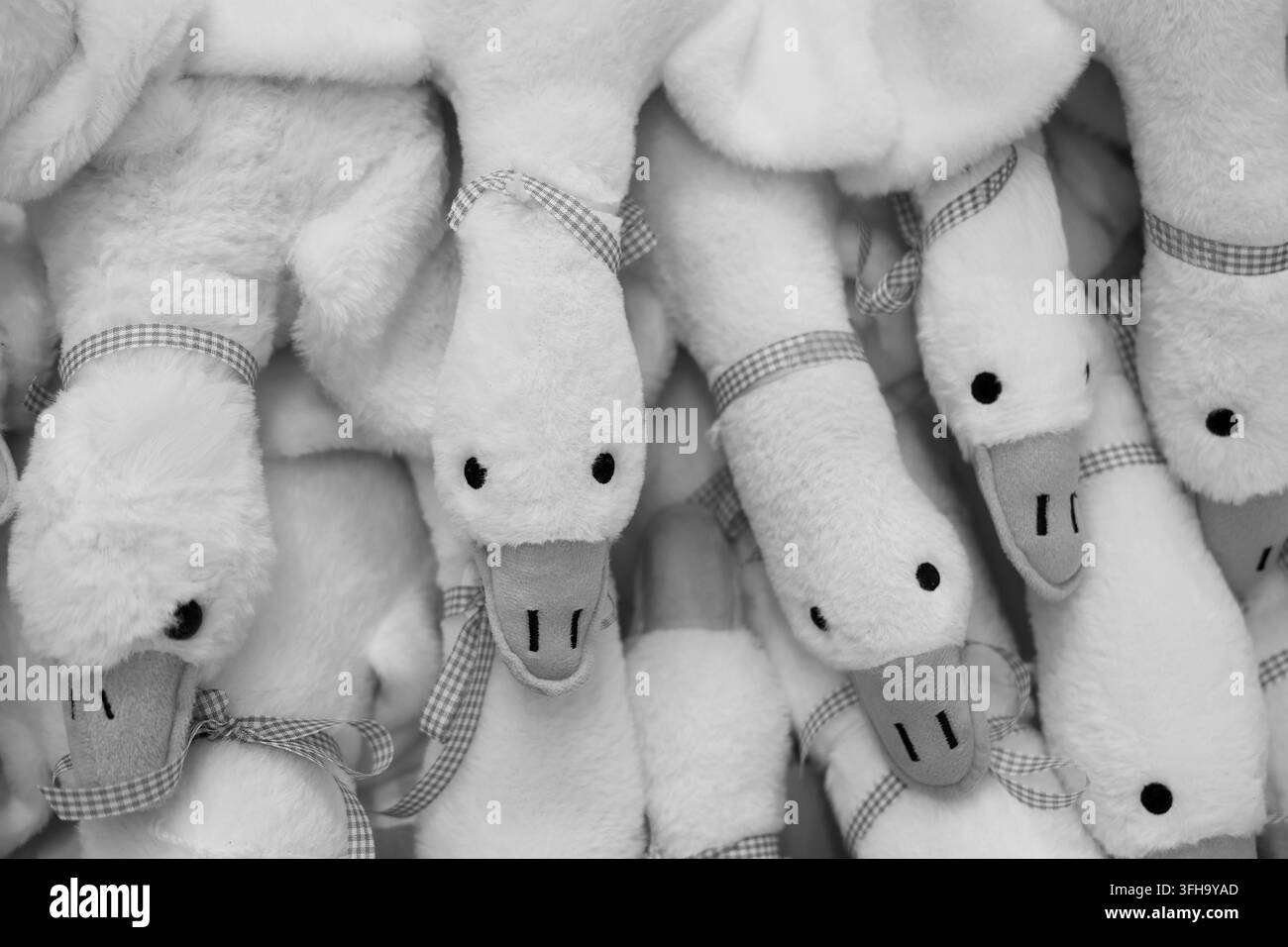 Un motivo di giocattolo di anatra di peluche in bianco e nero con tessuto morbido, dettaglio di nastro e disposizione giocosa che crea uno sfondo tessile allegro Foto Stock