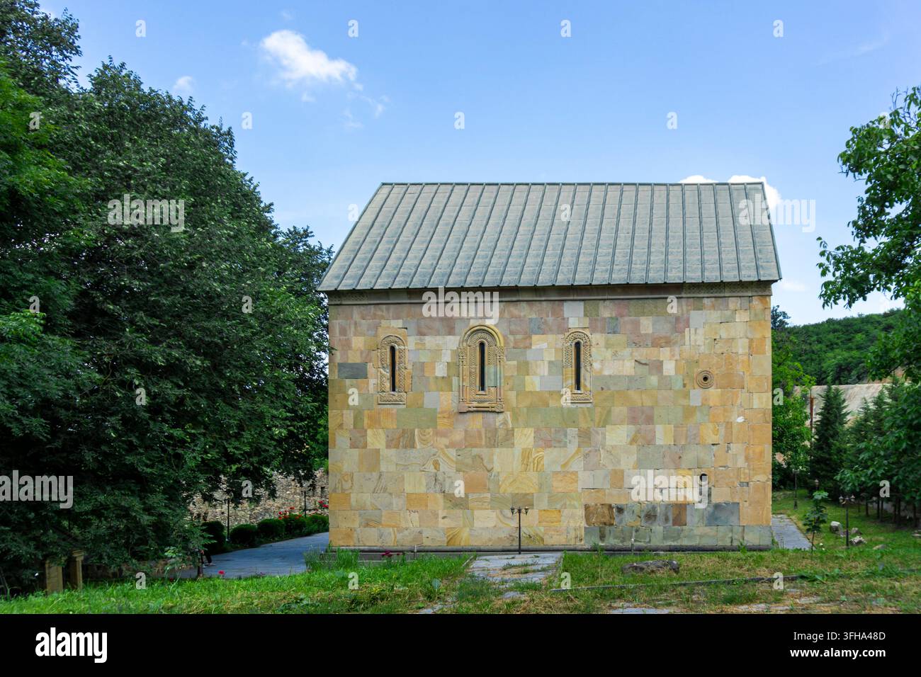 Chiesa della Santa Trinità vicino alla città di Kazreti. Mura di pietra chiara, un bellissimo giardino con alberi e fiori Foto Stock