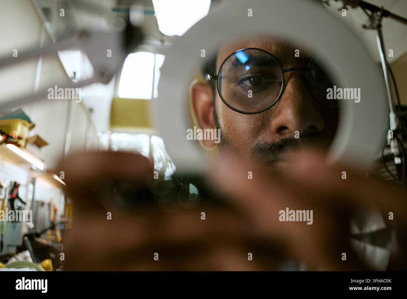Ritratto di un uomo indiano che ispeziona l'elettronica con una lente d'ingrandimento Foto Stock