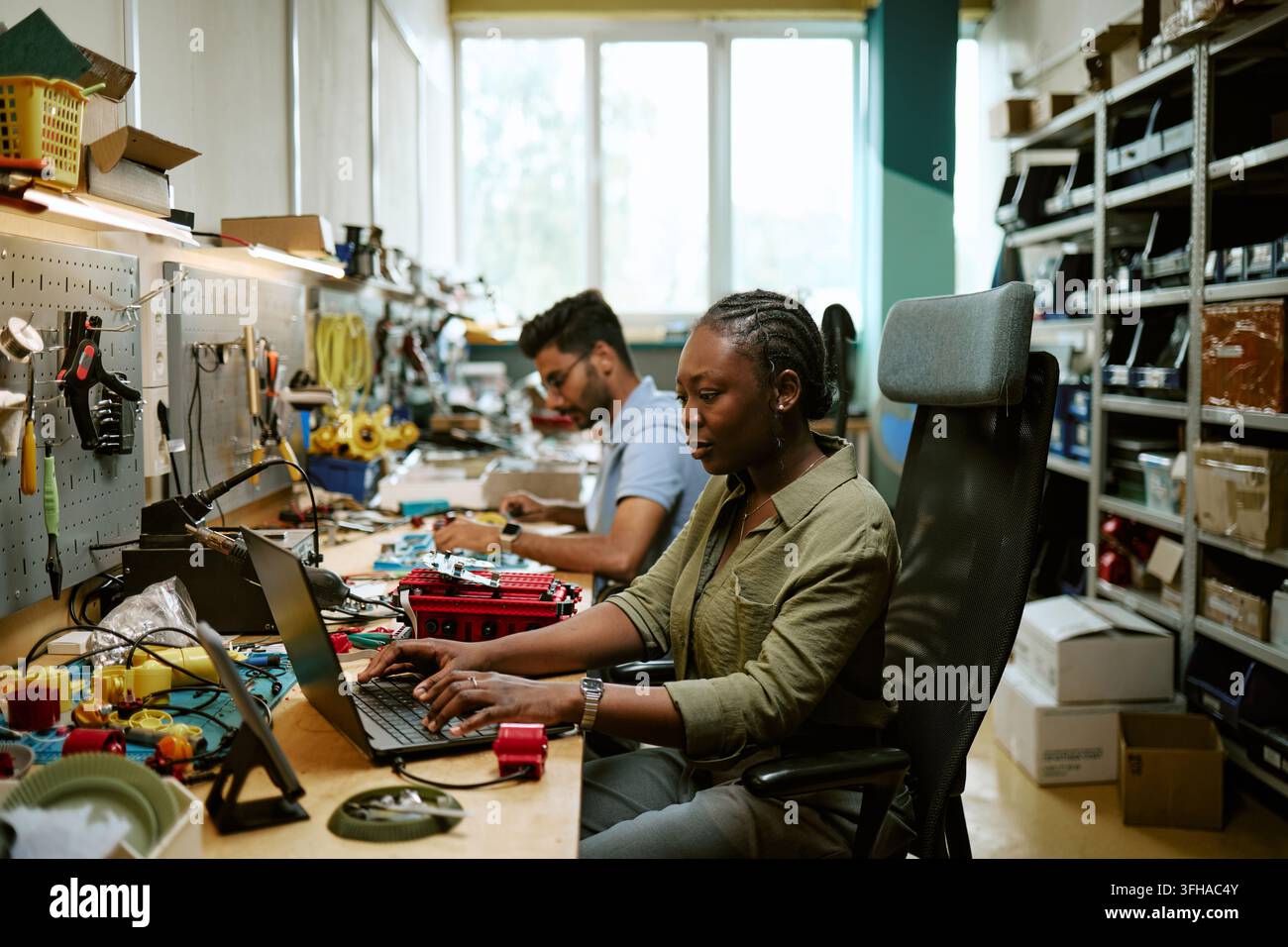 Ingegnera nera che digita su un laptop in un laboratorio di elettronica Foto Stock