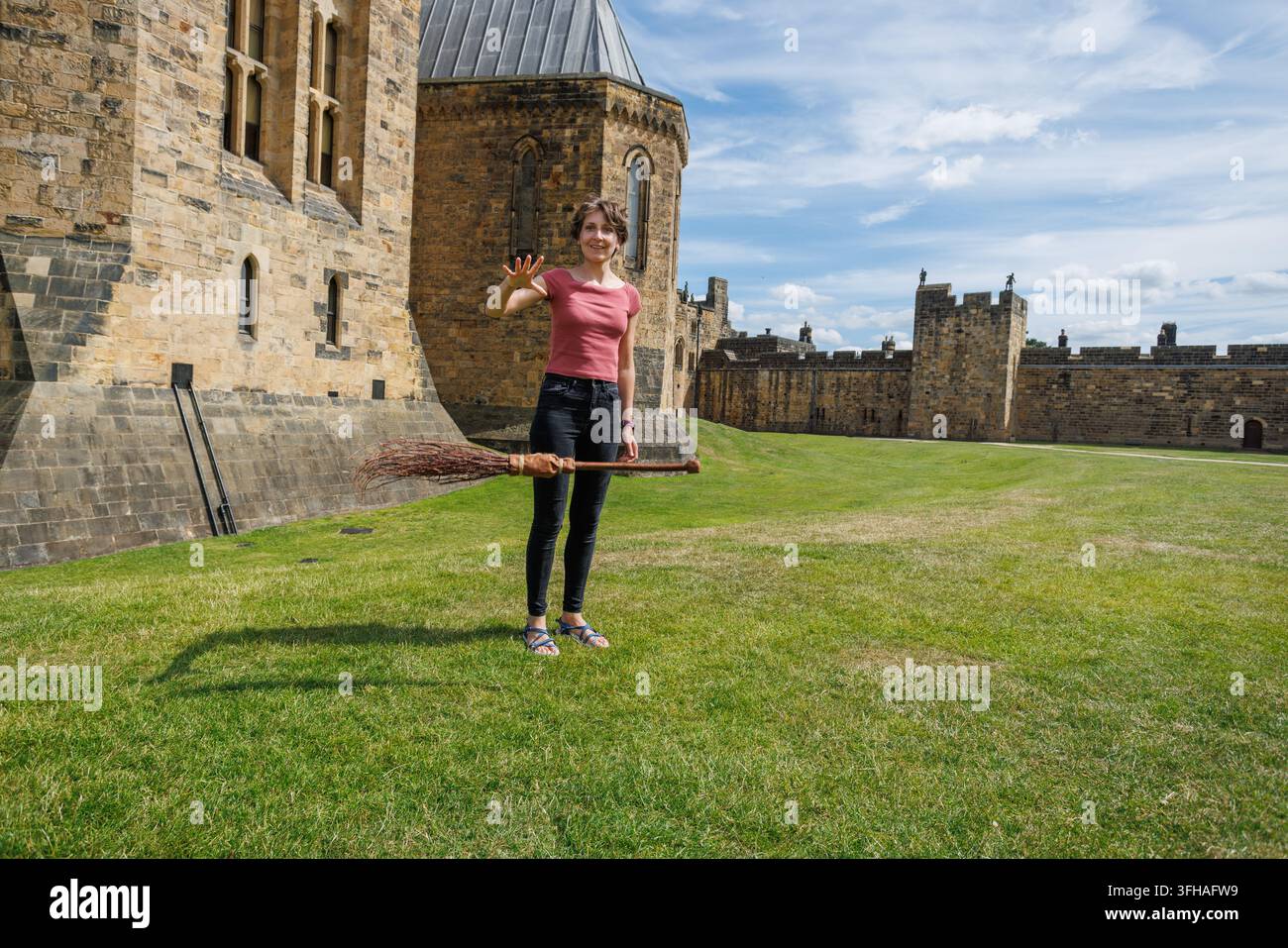 Giovane donna che finge di far volare una scopa in un castello storico Foto Stock