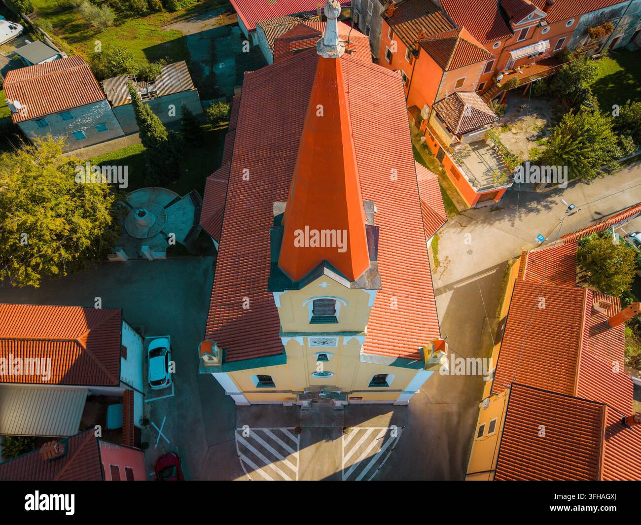 Vista aerea della Chiesa di San Zeno con il suo caratteristico tetto rosso e la facciata gialla circondata dai tetti storici del villaggio di Brtonigla, Istria Foto Stock