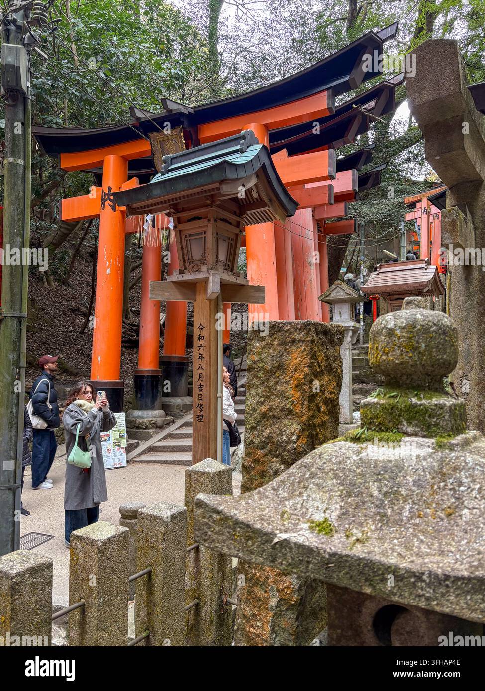 Turisti che scattano foto sotto enormi cancelli torii vermigli e lanterne di legno al Santuario di Fushimi Inari Taisha a Kyoto, Giappone. - Immagine stock catturata con smartphone