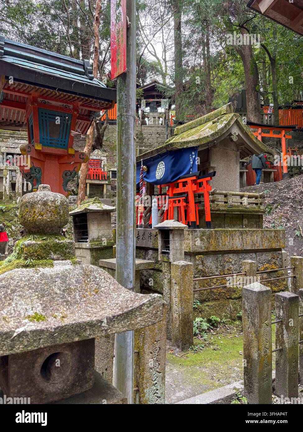 Lanterna di pietra muschiosa e piccolo altare del santuario con torii votivi in miniatura al Fushimi Inari Taisha a Kyoto, Giappone. - Immagine stock catturata con smartphone