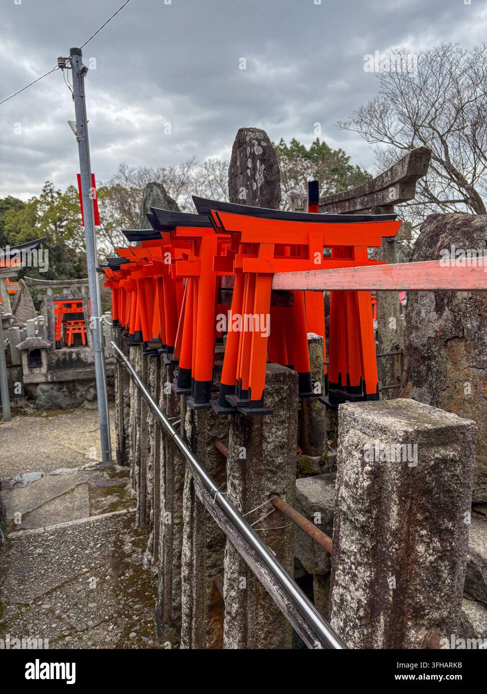 File di piccoli cancelli torii arancioni disposti come offerte votive lungo le ringhiere di pietra al Fushimi Inari Taisha a Kyoto, Giappone. - Immagine stock catturata con smartphone