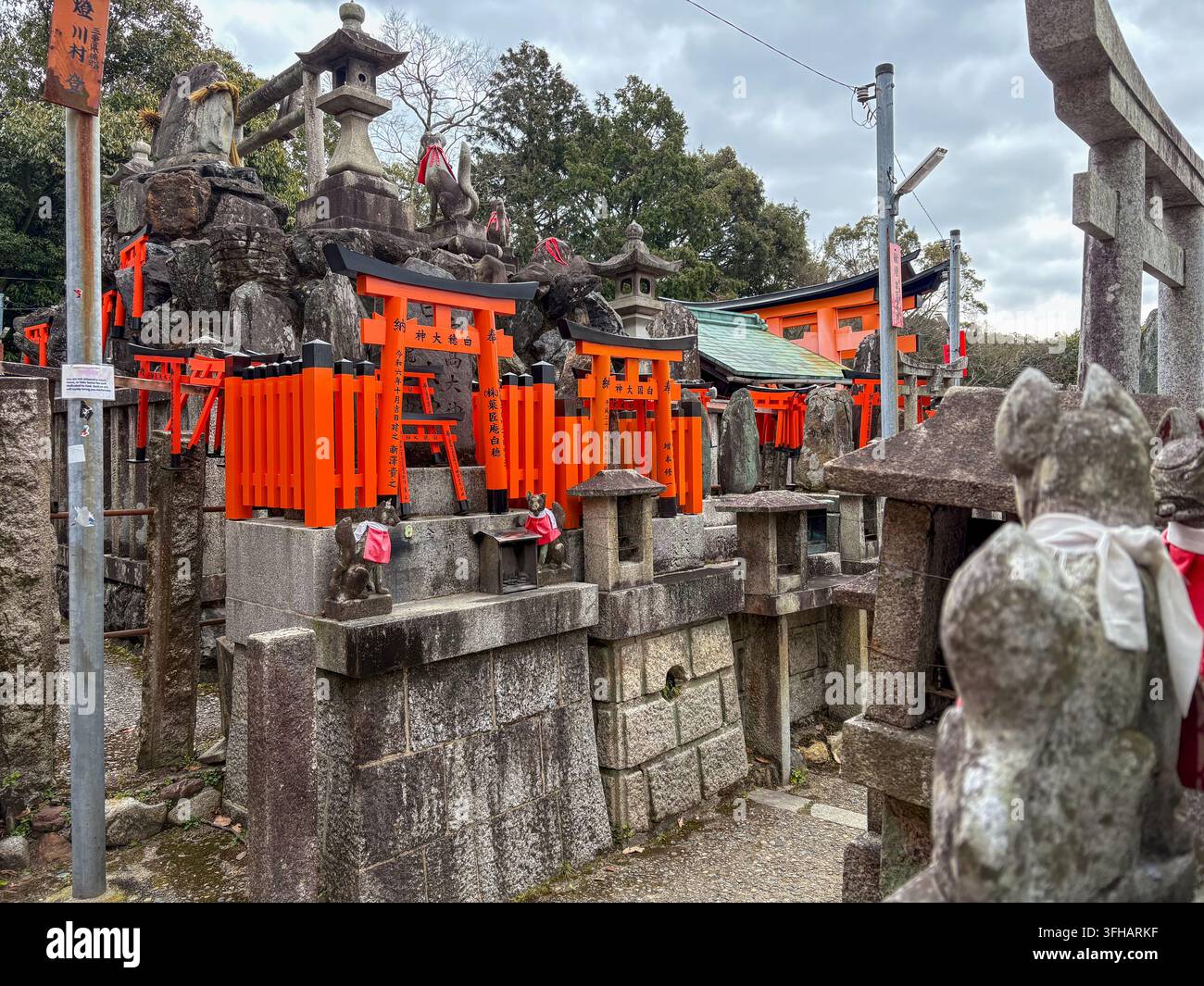 Altari di pietra sacri con statue di volpe in pietra e cancelli torii arancioni al santuario di Fushimi Inari a Kyoto, Giappone. - Immagine stock catturata con smartphone