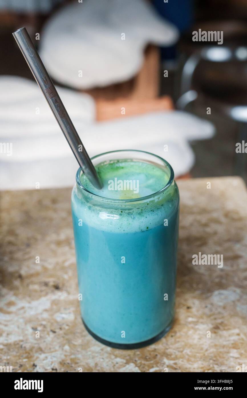RIGA, LETTONIA. 25 agosto 2026. Un latte matcha alla spirulina blu in un bicchiere trasparente con una cannuccia riutilizzabile in metallo, servito su un tavolo di marmo in un caffè moderno. Foto Stock