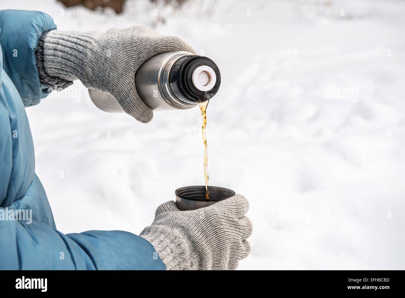 Versare una bevanda calda da una tazza termica all'aperto in inverno Foto Stock
