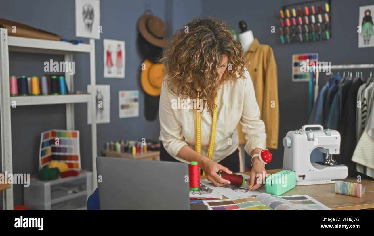 Sarta donna con metro a nastro tiene una bobina di filo rosso e regola il tessuto vicino alla macchina da cucire e al manichino in studio; focus creativo. Foto Stock