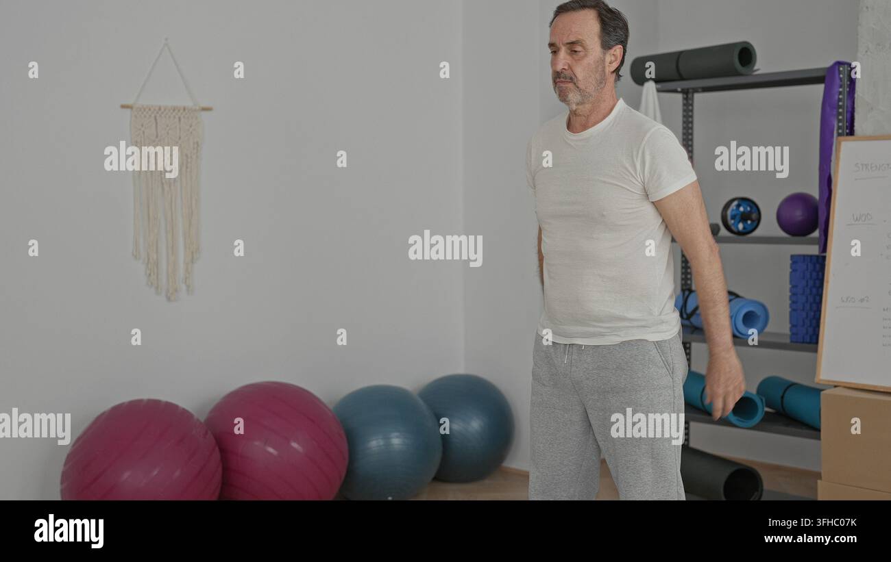 Uomo accovacciato con le mani unite sulle palle da esercizio in studio, che esegue uno squat di mobilità a basso impatto per lo stretching e l'equilibrio; enfasi sulla forza. Foto Stock