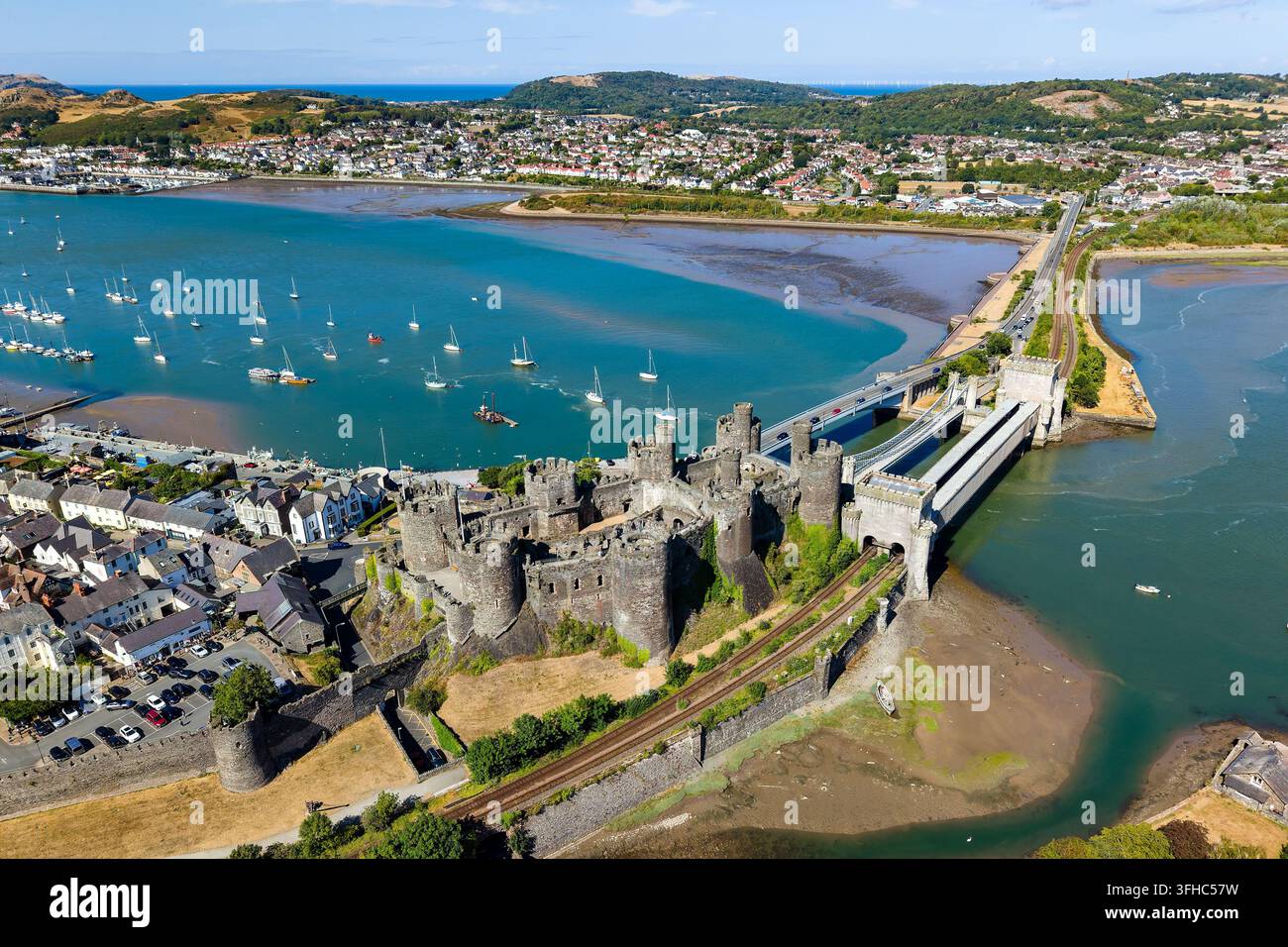 Vista aerea del castello di Conwy e dei ponti storici che attraversano il fiume Conwy nel nord del Galles, con barche ormeggiate sull'acqua blu dell'estuario, in una giornata estiva Foto Stock