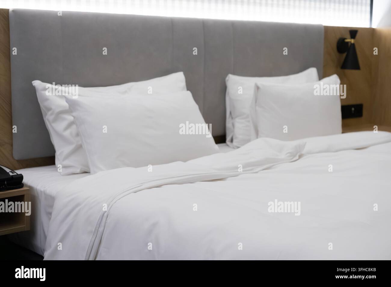 La suite d'albergo minimalista presenta un letto pulito con una biancheria da letto morbida e un'illuminazione ambientale, creando un'atmosfera accogliente progettata per il comfort di viaggio, r Foto Stock