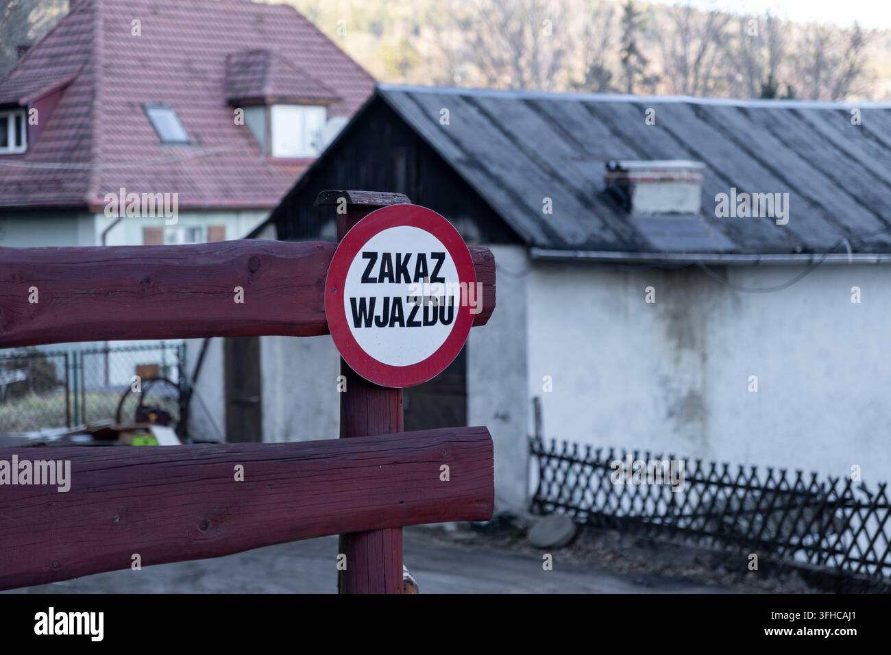 Un cartello stradale circolare rosso e bianco con la scritta ZAKAZ WJAZDU in polacco, che indica il divieto di ingresso, fissato a una barriera in legno resistente che protegge una residenza Foto Stock