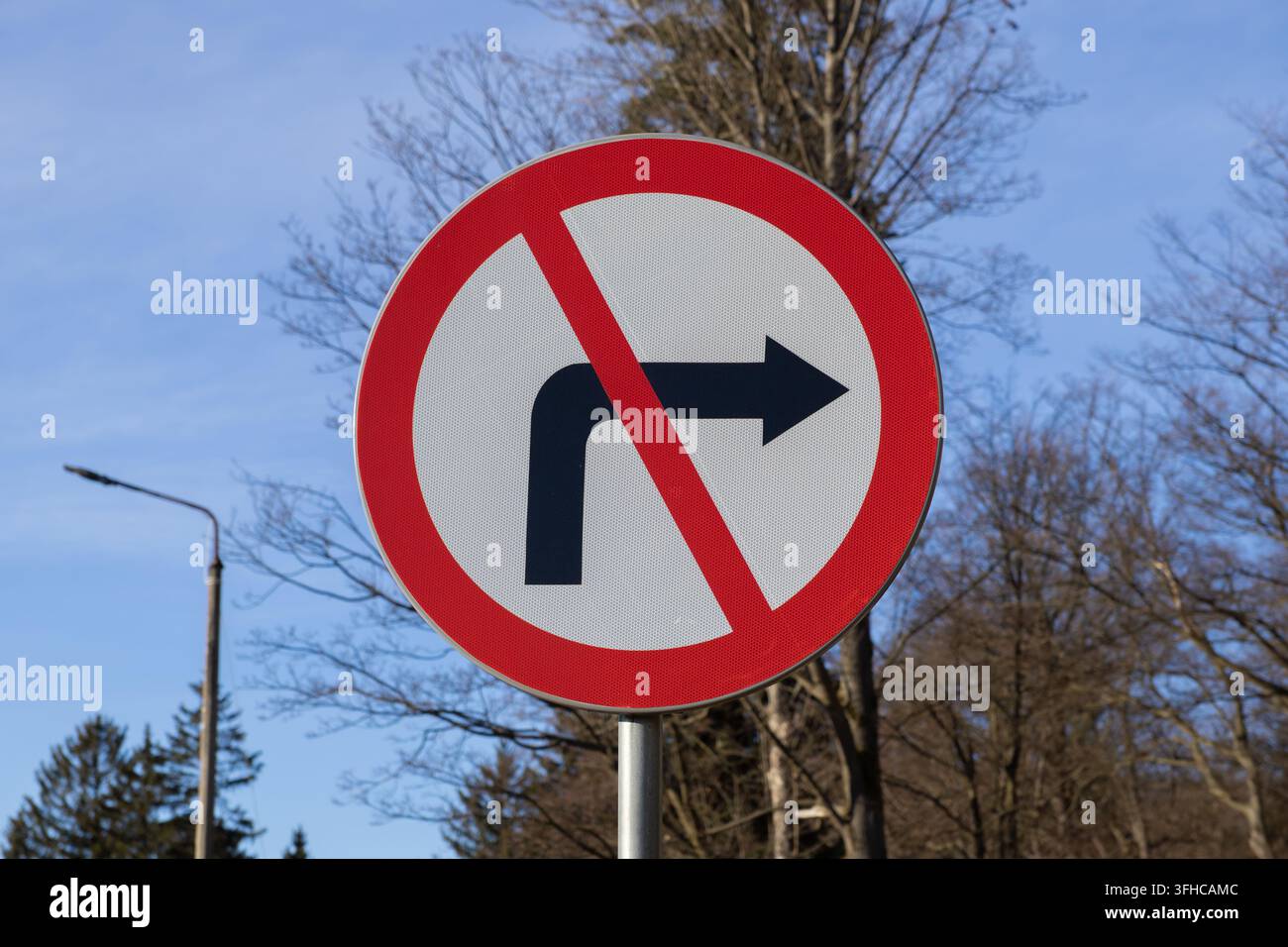 Primo piano di un cartello stradale circolare rosso e bianco riflettente che mostra chiaramente una freccia nera con una linea diagonale, che vieta una svolta a destra per la strada Foto Stock